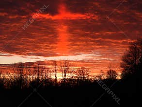 Cross outline in orange clouds of a late winter sunset before Easter