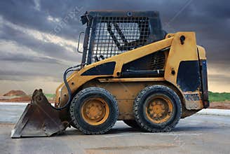 Skid Steer Loader On Construction Site Under Stormy Sky, Heavy Yellow Loader Vehicle