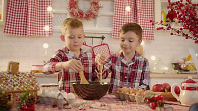 Cute boys making gingerbread dough together at the kitchen on Christmas eve