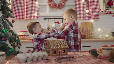 Cute boys decorating gingerbread house with topping and icing at the kitchen