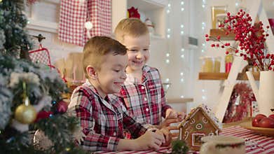Cute boys decorating gingerbread house with topping and icing at the kitchen