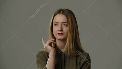 A young woman stands in front of the camera and holds her finger to her chin while trying to remember something. A young