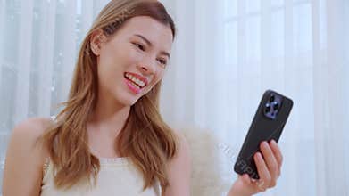 Young asian woman sitting on sofa using smart phone for video call in living room at home.