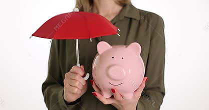 Woman holds pink piggy bank under red umbrella saving money