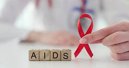 Doctor holds a red ribbon next to wooden blocks with inscription AIDS