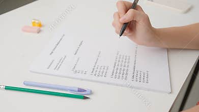 Female circles correct answers in standard math exam test paper with black pen. Student at desk filling up the answer