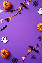 Halloween frame of bunting, ghosts, pumpkins, web, bats, spiders on purple background. Flat lay, top view, copy space