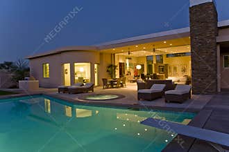 House With Sunloungers On Patio By Pool At Dusk