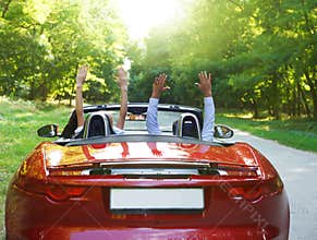 Happy free couple driving in red retro car cheerin
