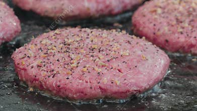 raw seasoned beef hamburgers on flat grill cooking close up