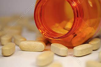 Yellow pills of vitamin C scattered on the table and open orange jar