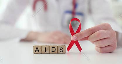 Doctor holding in his hands red ribbon symbol of fight against HIV and AIDS closeup
