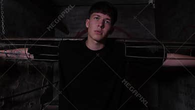 A young man is chained to horizontal handcuffs in a dark quest room.