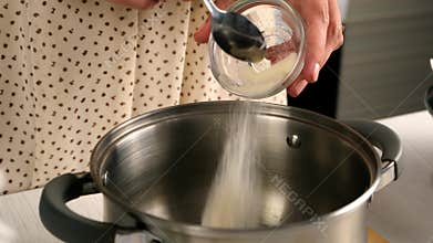 Woman cooking adding gelatin to water in pan on kitchen at home.