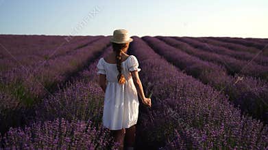 Girl is runs through a field of purple flowers. She is wearing a white shirt and a hat.
