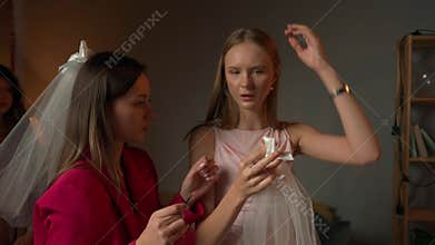 Group of young women friends and bride celebrating bachelorette party at home, girls helping each other with veils