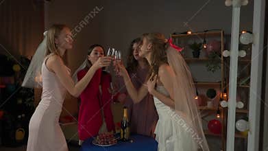 Group of young women friends celebrating bachelorette party at home, bridesmaids and bride talking, drinking champagne