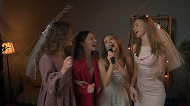 Group of young women friends and bride celebrating bachelorette party at home, bride and bridesmaids having fun, singing