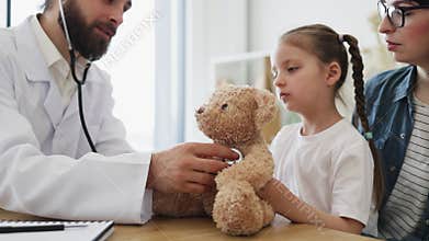 Friendly doctor demonstrates stethoscope checkup with teddy bear for child