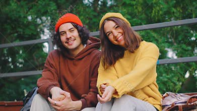 A smiling man and woman in colorful knitted hats and cozy sweaters are surrounded by vibrant greenery, capturing a