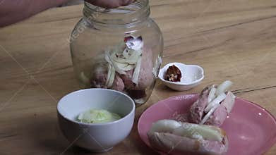 A man places sausages, onion, and pepper into a jar. He is preparing marinated sausages. Close-up