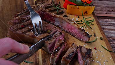 T- bone steak cut into pieces with a knife on a cutting board. Close up