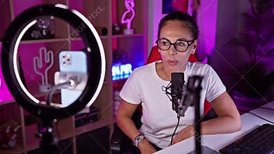 Hispanic woman podcasting with microphone in a neon-lit gaming room at night