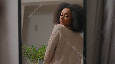 Unhappy African American woman looking in mirror reflection at home wear jumper casual style unhappy bad choice clothes