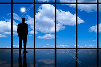 Business Man looking out of high rise office window at blue sky bright sunshine and white clouds.
