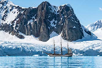 Mountain landscape with Tall Ship Bark Europa on expedition in Antarctica.