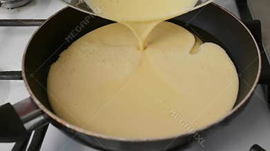 Pouring beaten eggs on hot frying pan with oil, close up