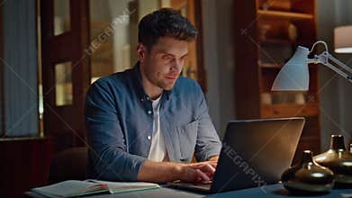 Smiling businessman browsing computer texting email at cozy dark flat closeup