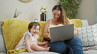 Smiling mother and daughter enjoying a relax moment, sitting on their living room sofa, exploring the internet on their laptop,