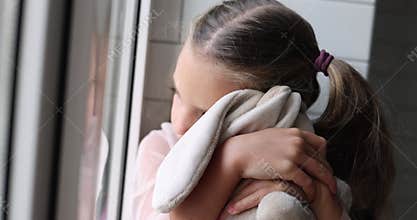 Bored girl sits on windowsill leaning on soft toy hare