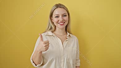 Cheerful young blonde woman, standing against a yellow isolated background, flashing a cool \'okay\' sign with a confident smile,