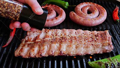 Chef Sprinkles Salt And Spices on pork ribs On Grill Rack. Cooking natural sausage on grill. Slow motion.