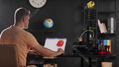 A graphic designer uses a laptop and makes a sketch of human heart in red colour, depicted on a device monitor. The