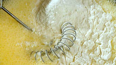 Close-up of pouring flour into a bowl with beaten egg and sugar to make batter.