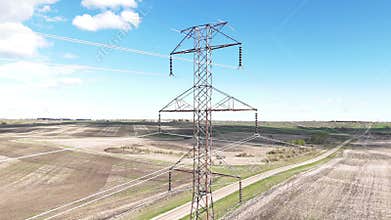 Power lines rising shot above farm lands and country road overlooking electrical pylon with transmission lines.