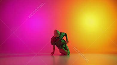 Cool attitude young man, talented freestyle dancer dancing in neon light against gradient pink-yellow background.