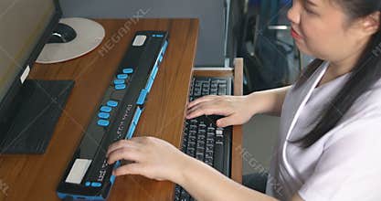 Asian woman with blindness disability using computer with refreshable braille display or braille terminal a technology assistive