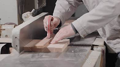 A man carpenter processes wooden planks on a benchtop of grinding machine, holds in hands and uses a jointer while