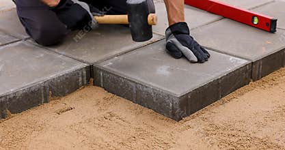 worker installing concrete paving slabs with rubber hammer