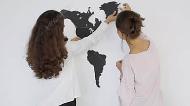 Two women assemble black cardboard world map on