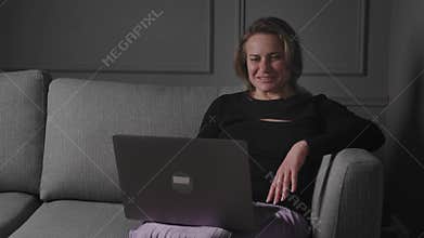 A woman is relaxing on the couch at home using her laptop for browsing and work