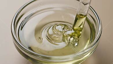Dropping Essential Oil into Aloe Vera Gel in Glass Bowl for Skincare Product Creation Under Bright Studio Lights Close