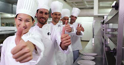 Smiling chefs standing in a row giving thumbs up