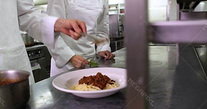 Chef serving up spaghetti and another garnishing with basil leaf