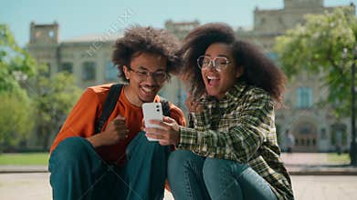 Two happy African American students celebrate good news mobile phone outdoor multiracial friends woman girl female man