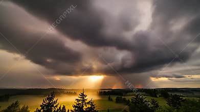 Sunset Over a Cloudy Landscape With Trees in the Foreground and Light Breakin